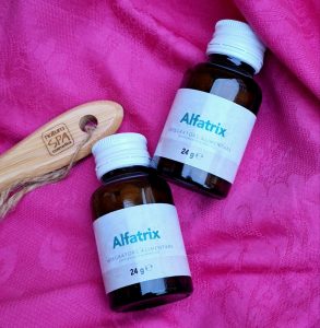 2 envases de alfatrix al lado de un cepillo de cabello de madera sobre fondo rosa
