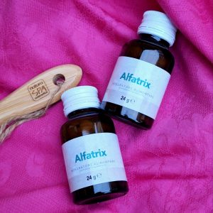 2 envases de alfatrix al lado de un cepillo de cabello de madera sobre fondo rosa